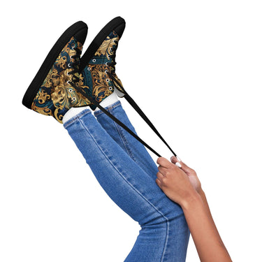 Woman wearing stylish high-top sneakers with baroque pattern, blue jeans, and holding up legs against a white background.